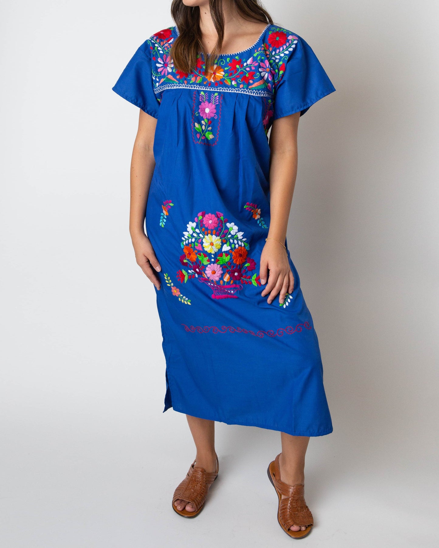 A woman wearing a traditional Mexican blue embroidered dress with colorful floral patterns.