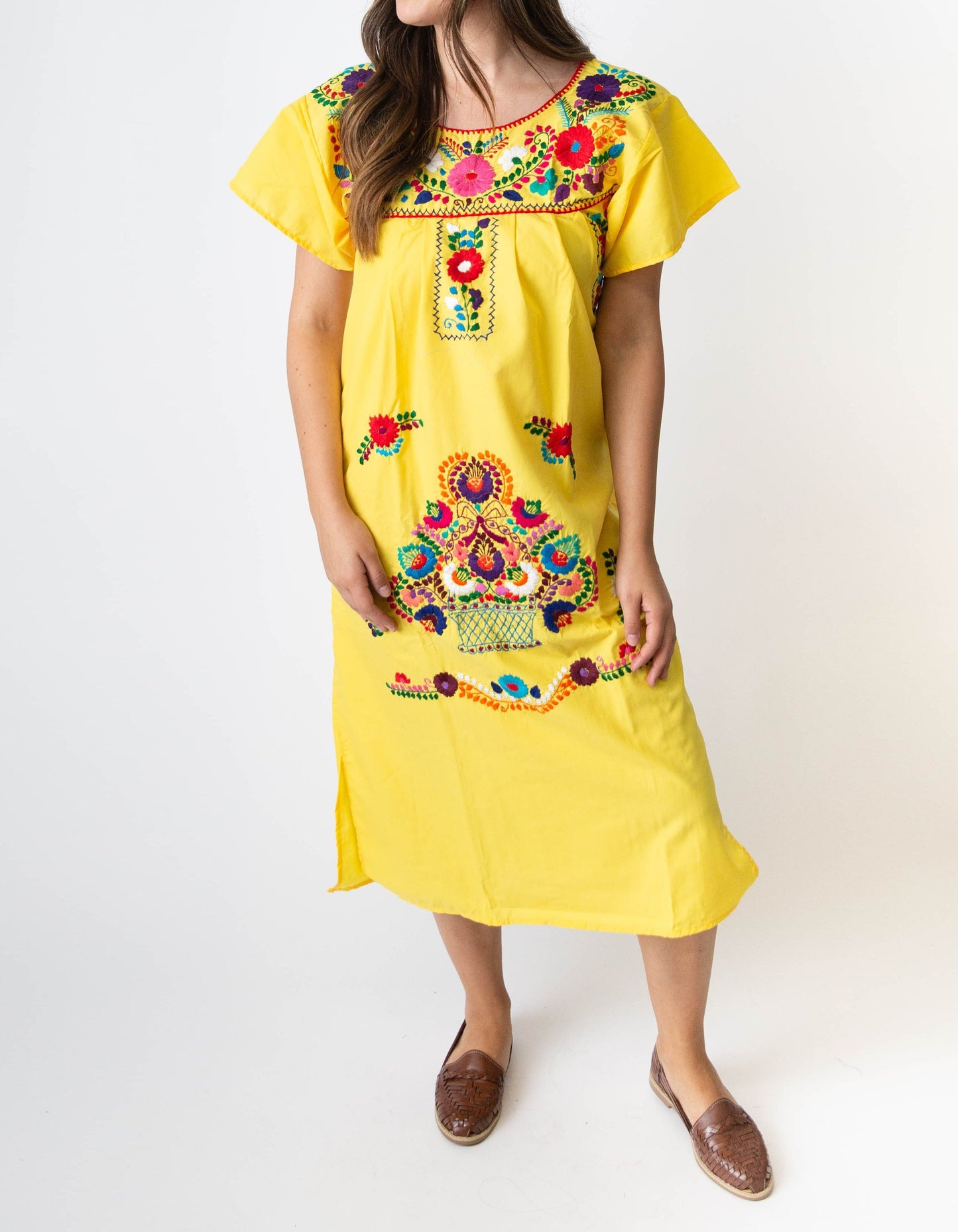 A woman wearing a traditional Mexican yellow dress with colorful embroidery.